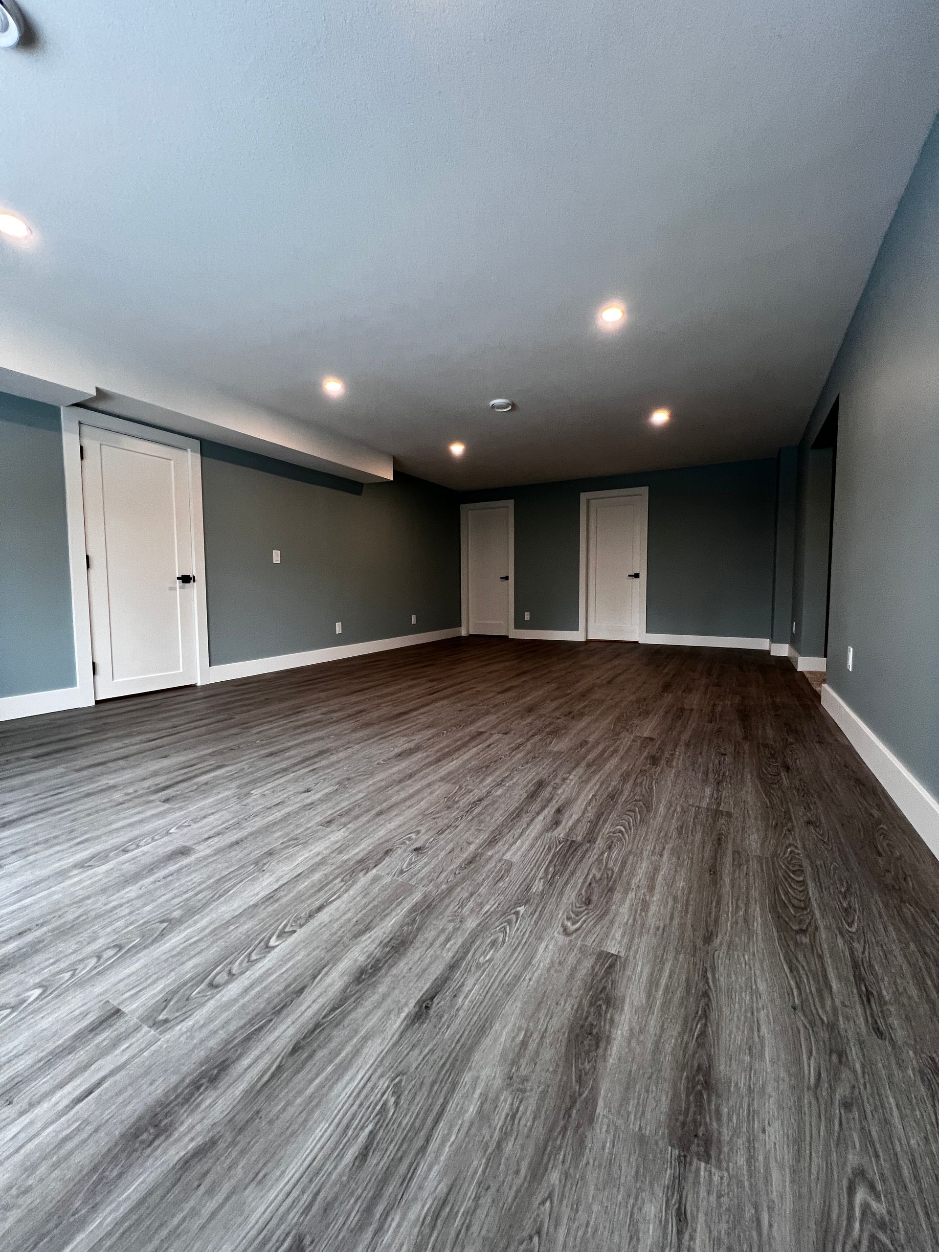 Basement suite with blue walls, dark grey/brown vinyl plank flooring, white interior doors, trim/baseboard, recessed lighting