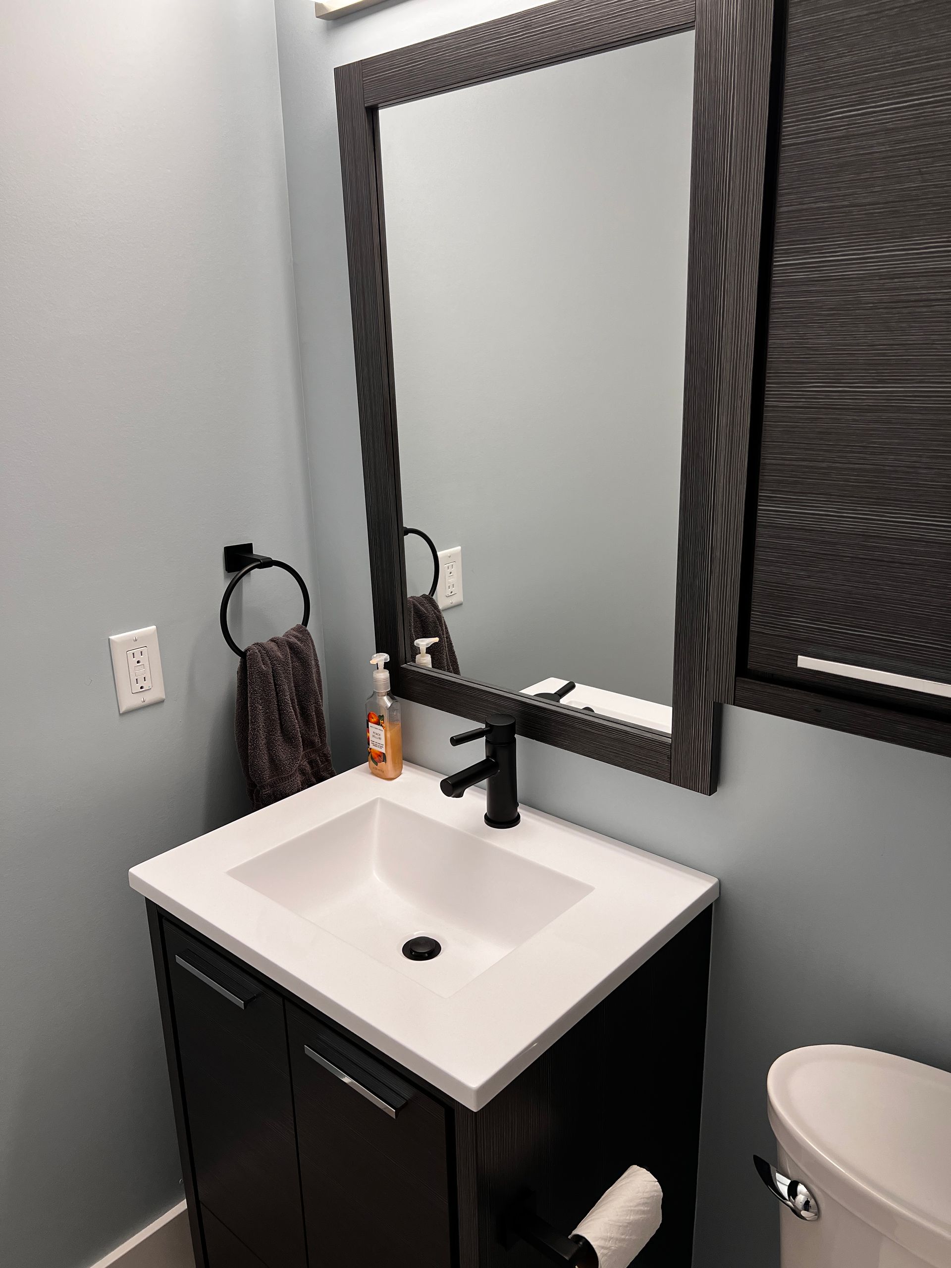Bathroom vanity sink with black faucet, wood trim mirror, hand-towel, medicine cabinet and blue walls.