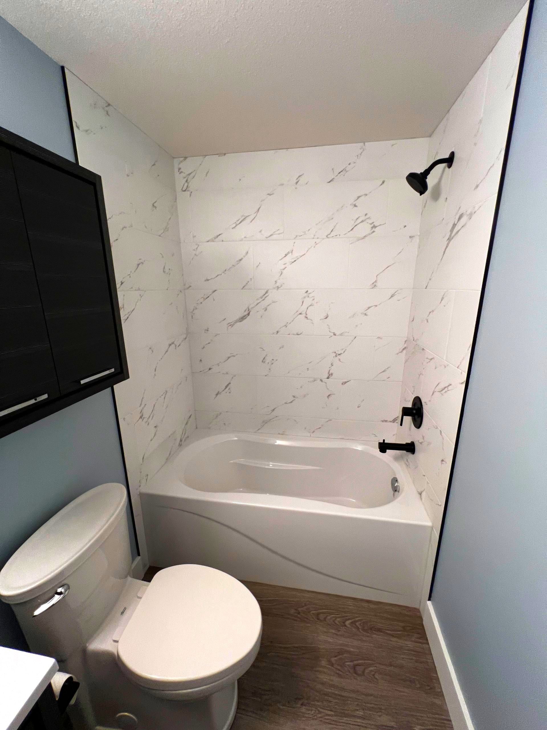 Bathroom with blue walls, a bathtub, white tile shower walls, tile edge, black shower trim, medicine cabinet and a toilet.