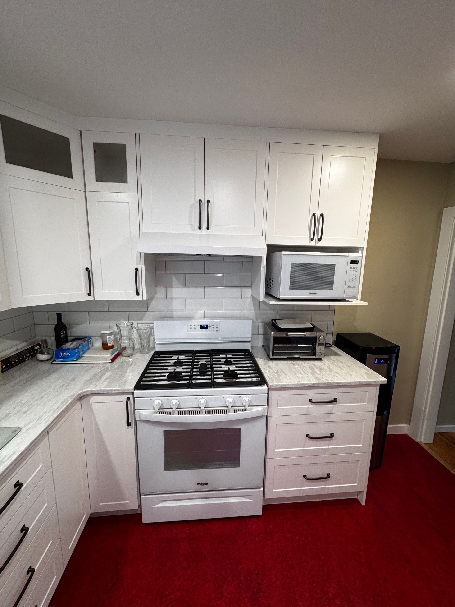White kitchen cabinets with white quartz countertop, white appliances, oven, range hood and microwave.