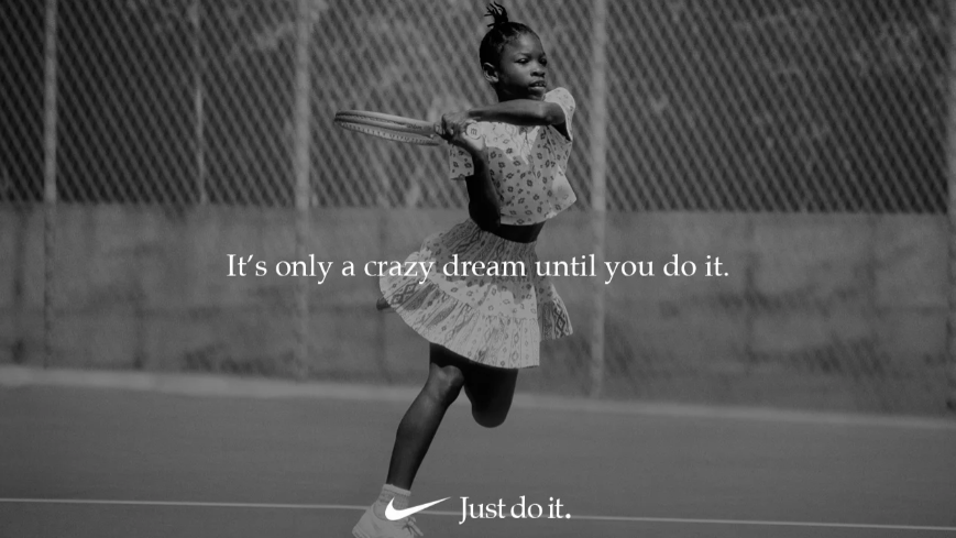 A black and white photo of a little girl holding a tennis racquet on a tennis court.