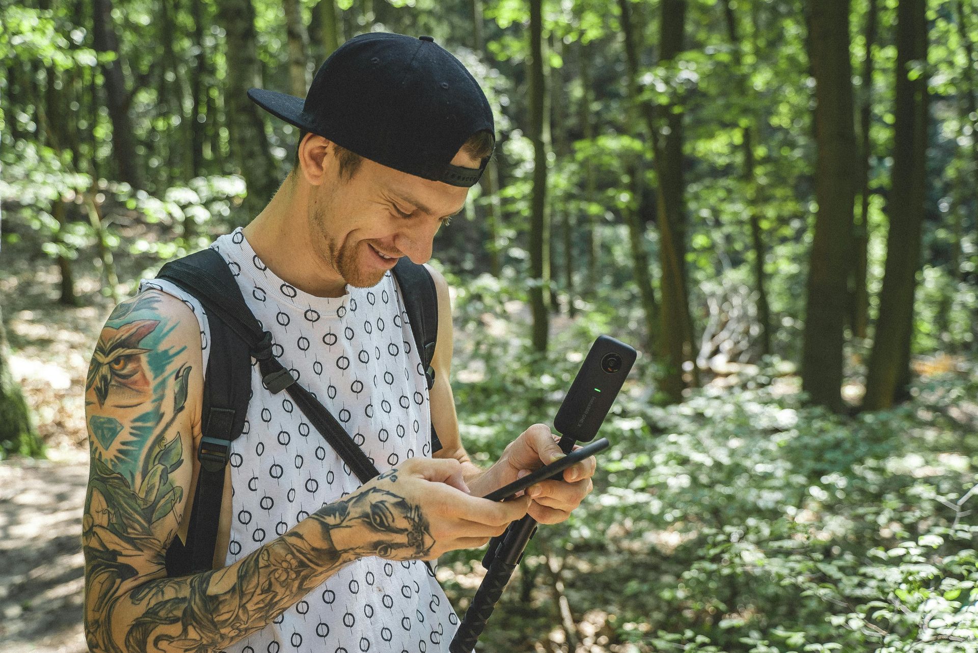 A man with tattoos is looking at his cell phone in the woods. A man with tattoos is looking at his cell phone in the woods.