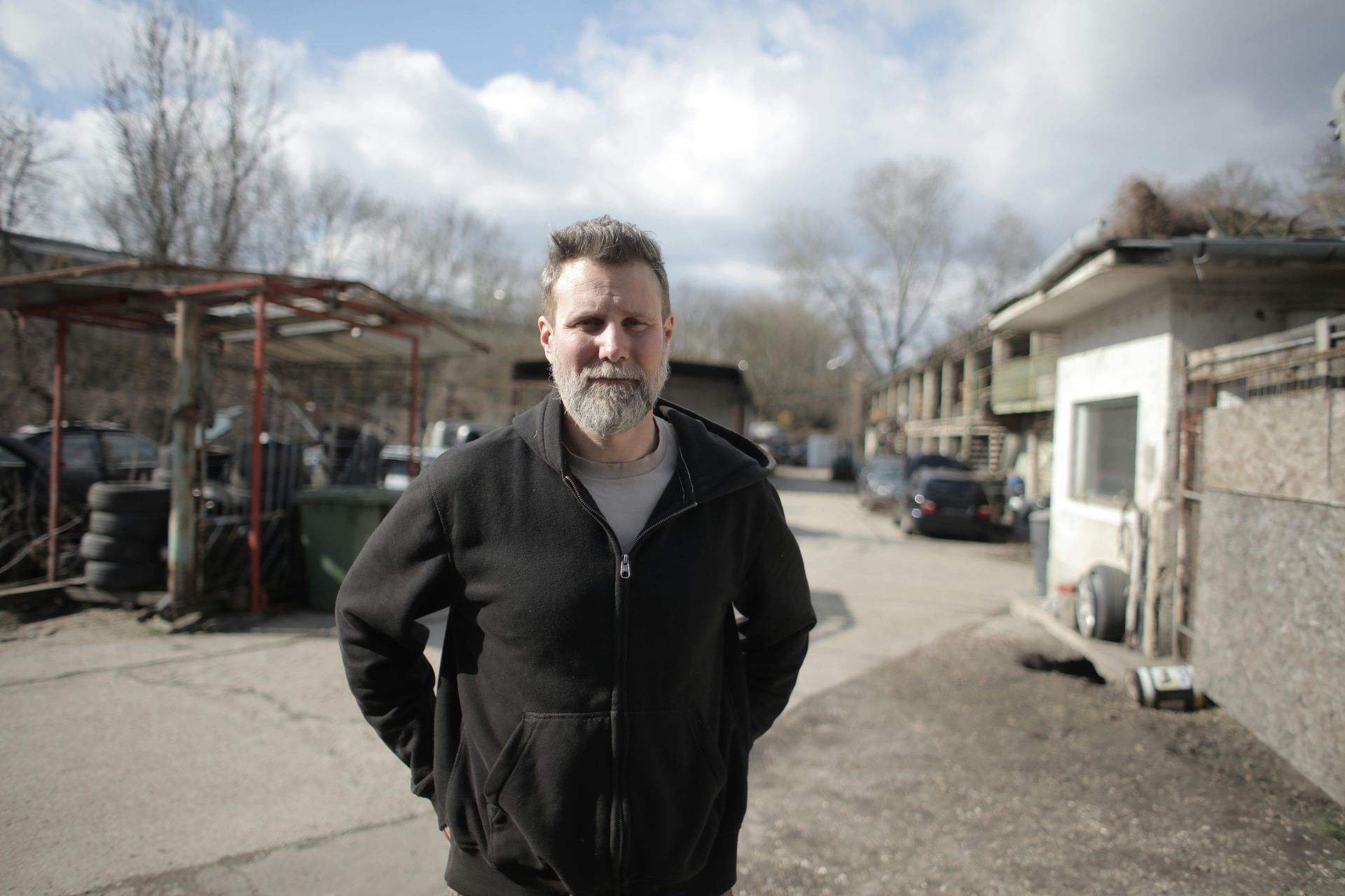 A man with a beard is standing in a parking lot with his hands in his pockets. A man with a beard is standing in a parking lot with his hands in his pockets.