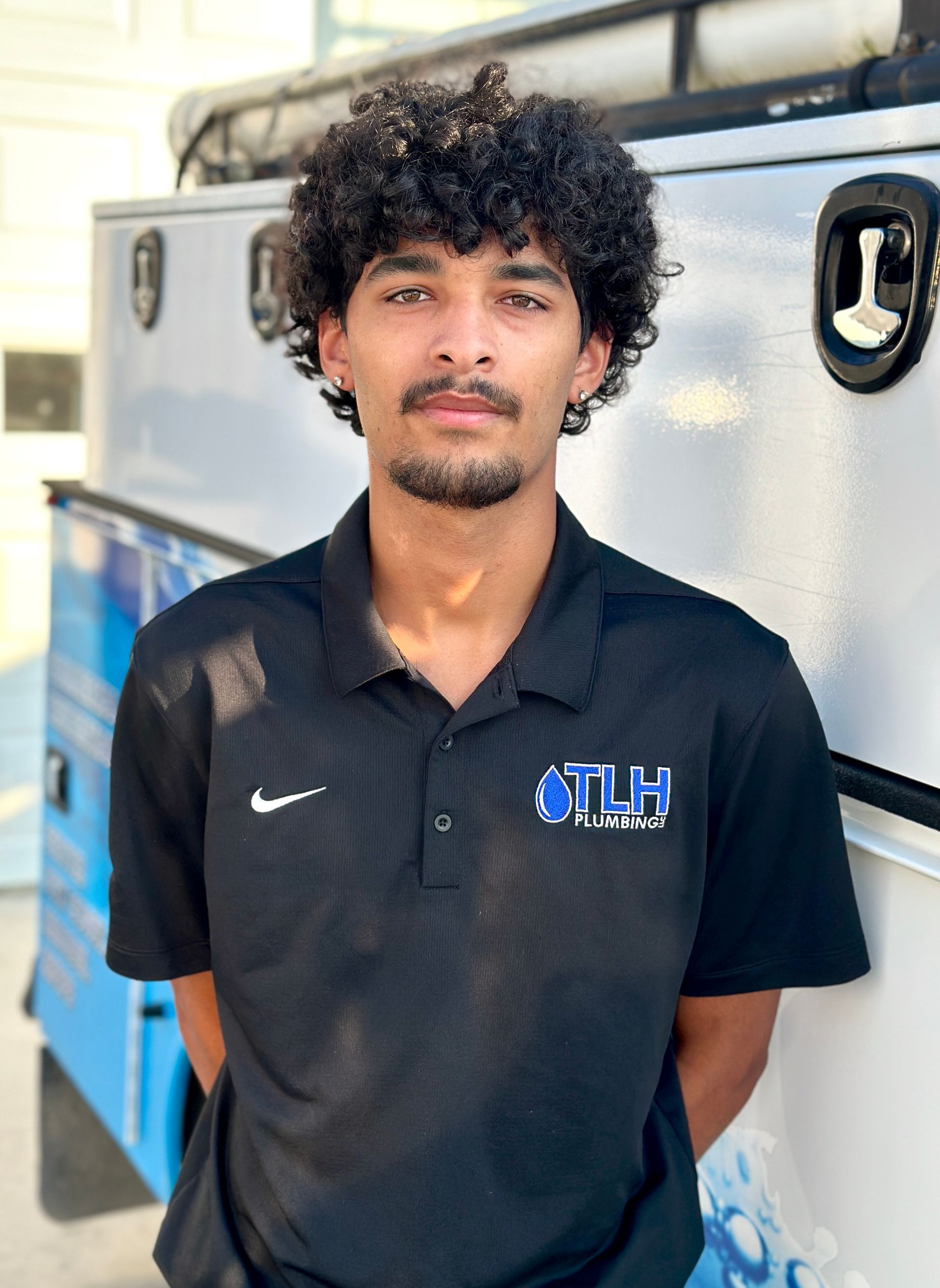 Man in black polo shirt stands in front of a white truck, looking at the camera.