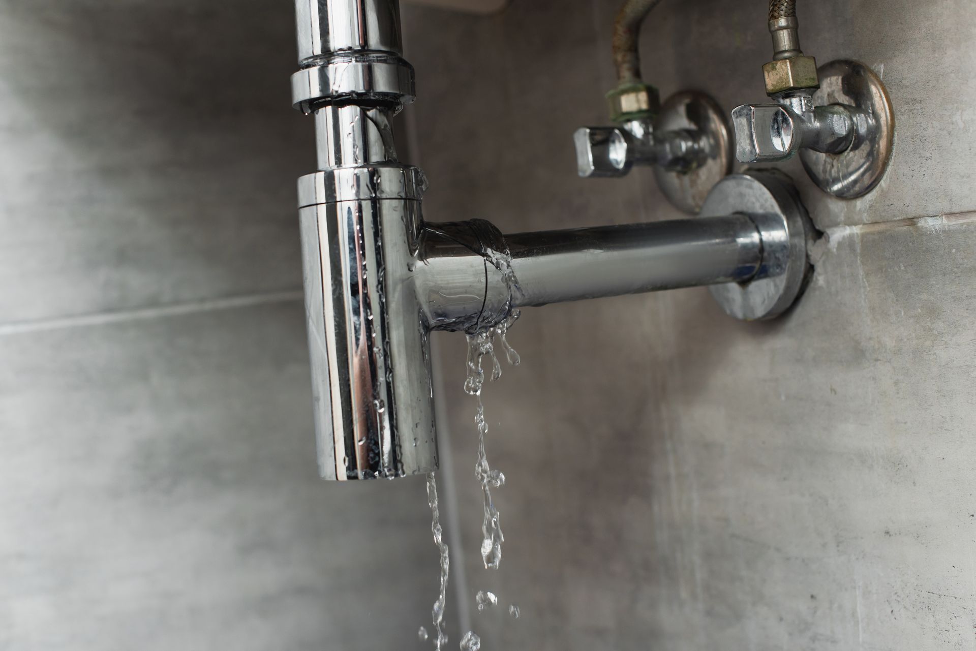 Chrome bathroom faucet leaking water against a gray tiled wall