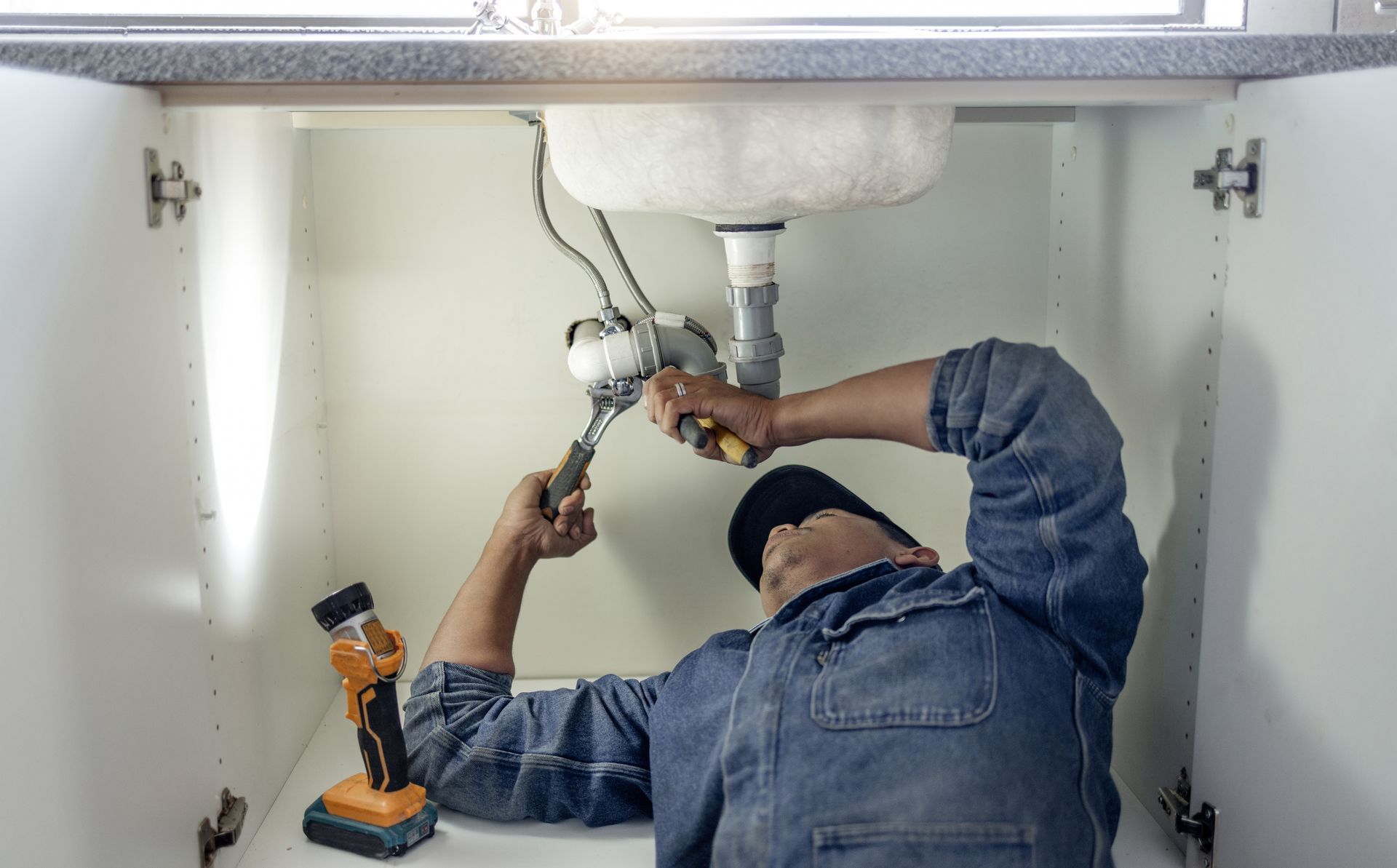 A plumber is fixing a sink in a kitchen.