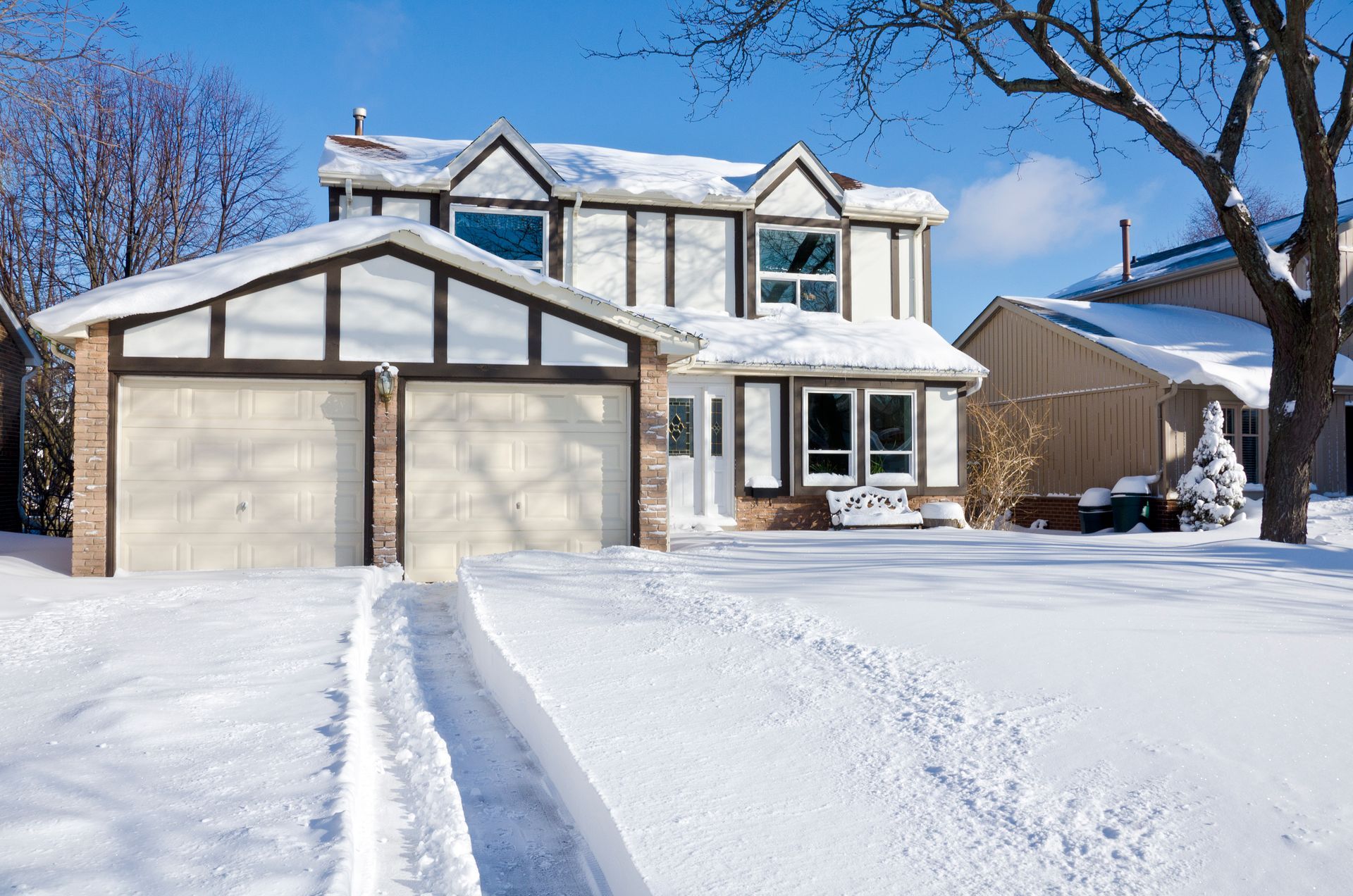 House covered in snow, with a two-car garage. Snow-covered driveway leads to the street.