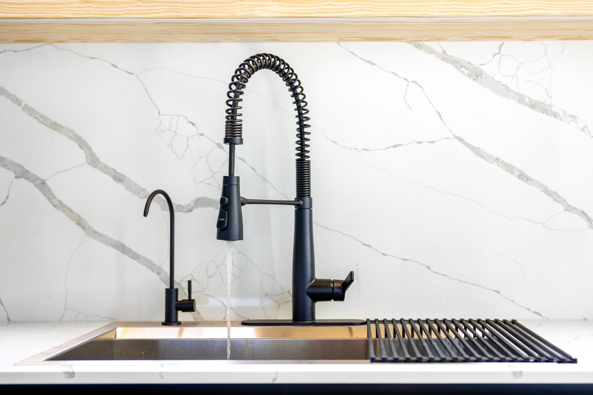 Black kitchen faucet with water running, in front of marble backsplash.