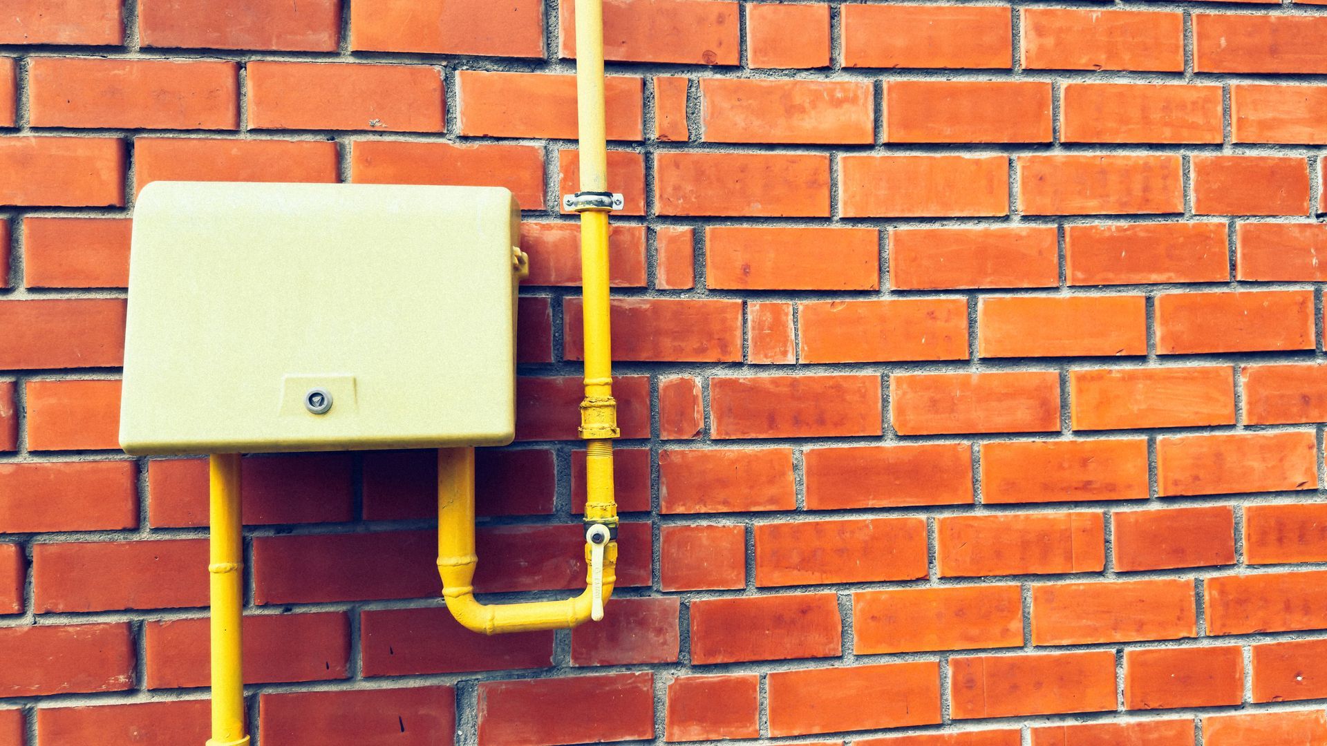 Yellow gas meter and piping on a red brick wall.