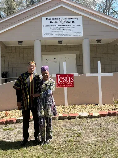Couple in front of a church, wearing matching patterned clothing, a white cross, and a 