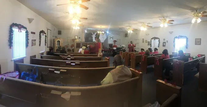 Inside a church, people seated in pews, Christmas decorations, and a speaker on a stage.