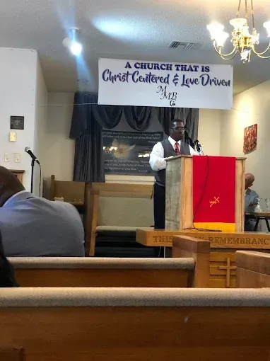Man speaking at a podium in a church. Banner reads 