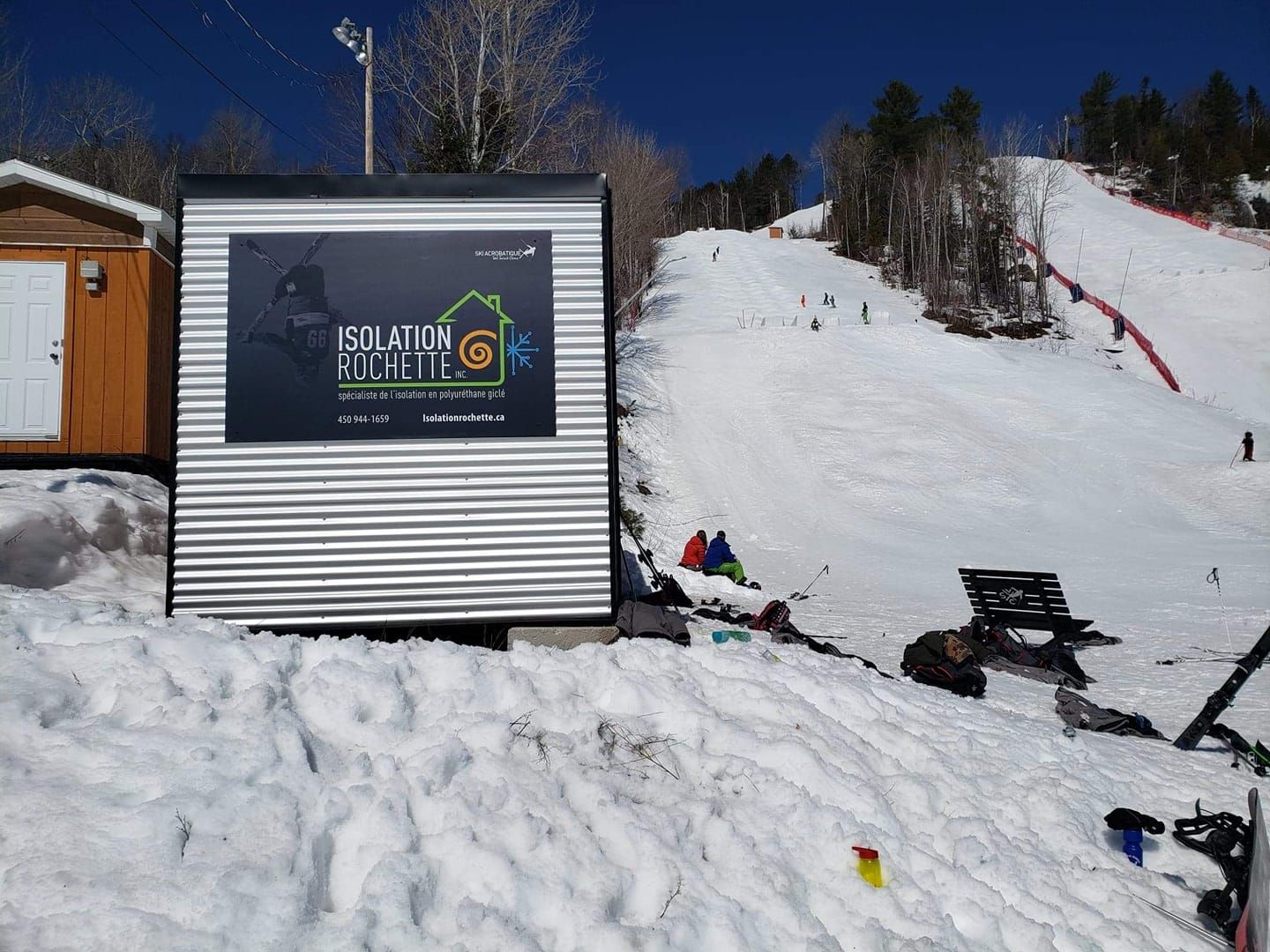 Panneau dans une station de ski avec des skieurs sur une pente, colline enneigée, journée ensoleillée.
