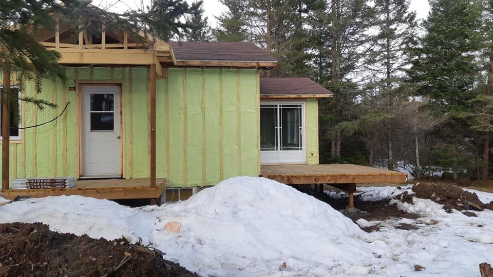 Maison en construction avec revêtement vert, porte blanche et un tas de neige.