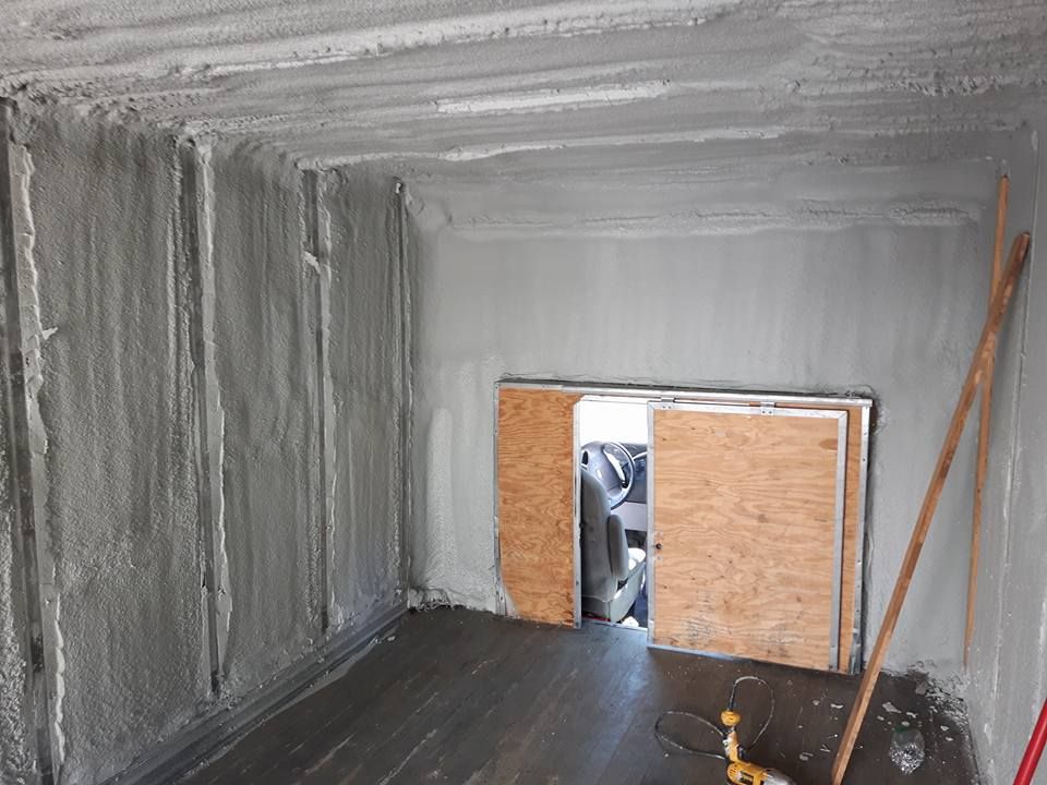 Intérieur d'un conteneur de fret avec isolation grise. Porte et plancher en bois visibles.