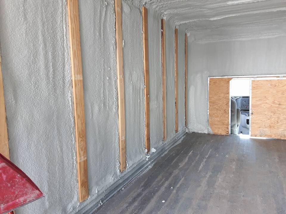 Vue intérieure d'une pièce avec isolation en mousse grise sur les murs avec poutres en bois et portes en panneaux de bois.