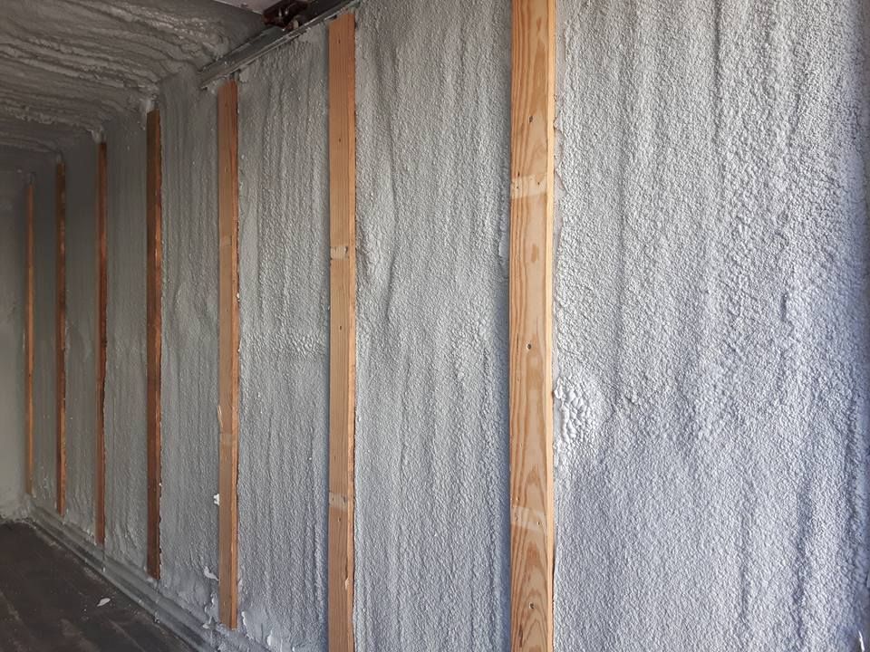 Isolation en mousse projetée à l'intérieur d'une structure, recouvrant les murs et les poutres en bois.