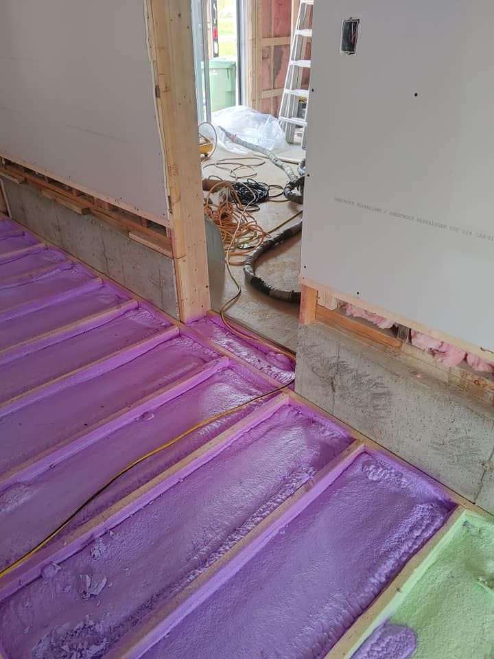 Isolant en mousse pulvérisée violette remplissant les solives de plancher d'un bâtiment en construction.