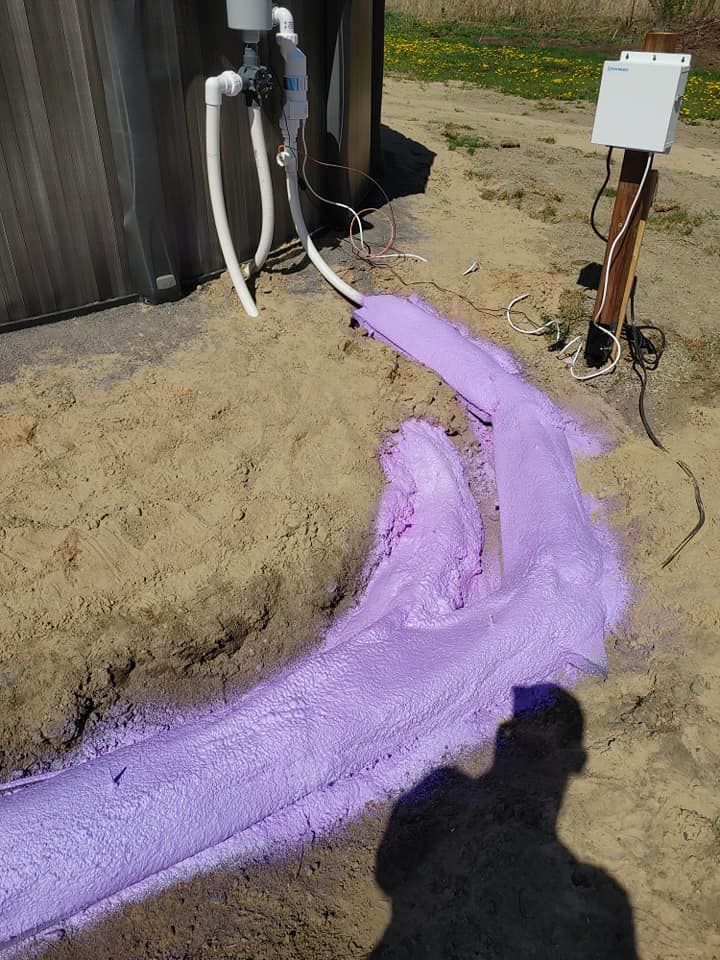 Mousse violette se déversant d'un réservoir sur du sable, près d'un poteau en bois et de tuyaux.