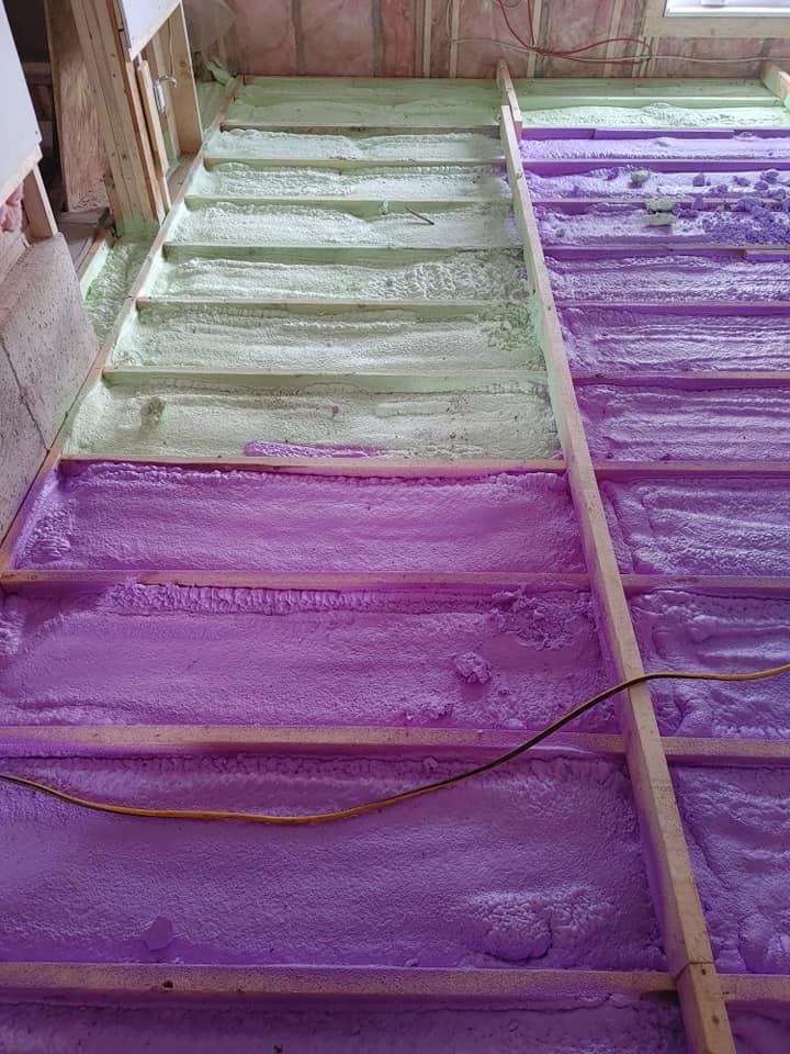 Isolation en mousse pulvérisée rose et verte entre les poutres en bois dans une cavité murale.