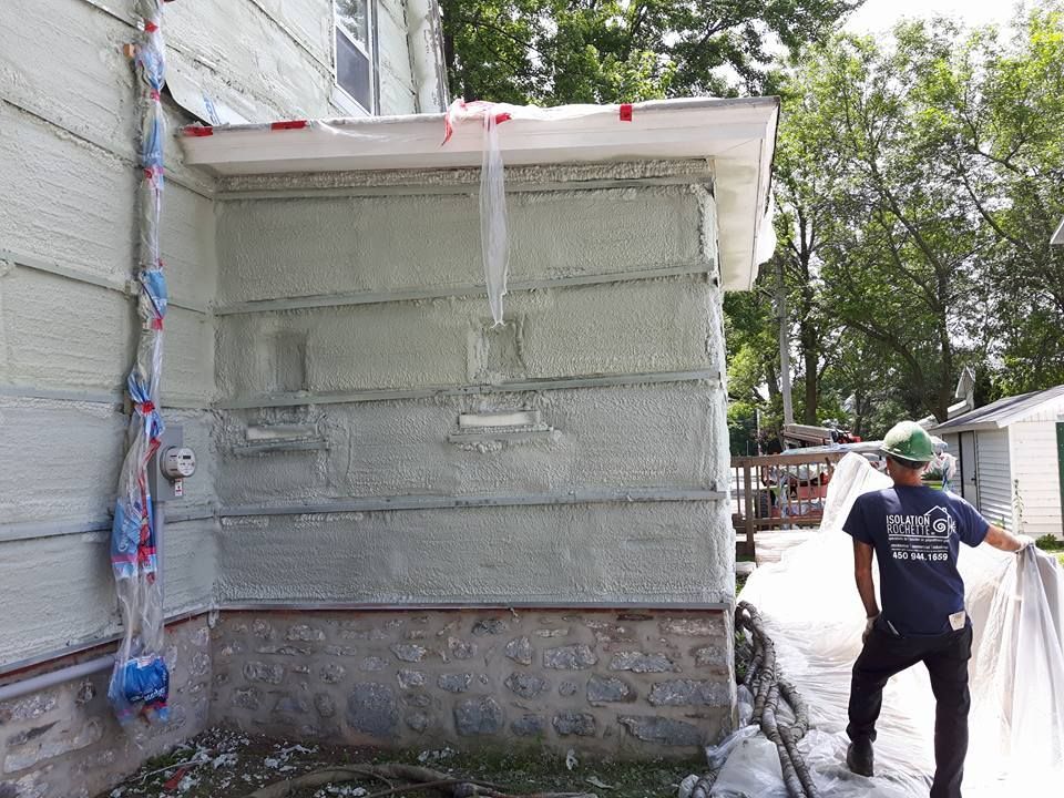 Mur extérieur avec isolation appliquée, ouvrier du bâtiment tenant une bâche.