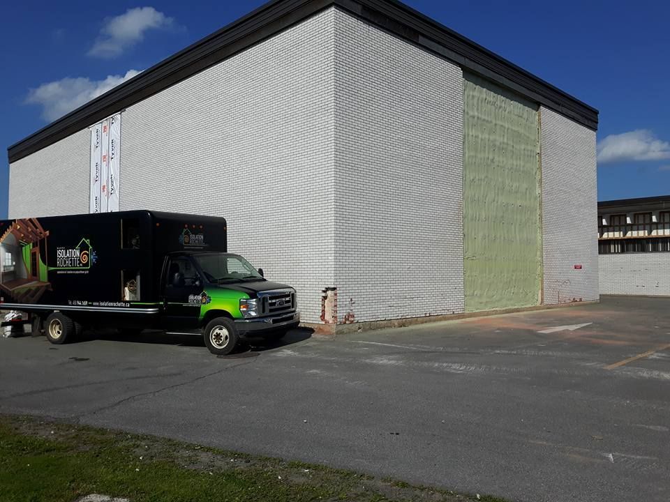 Un camion noir avec le logo d'une entreprise garé à côté d'un bâtiment en travaux.