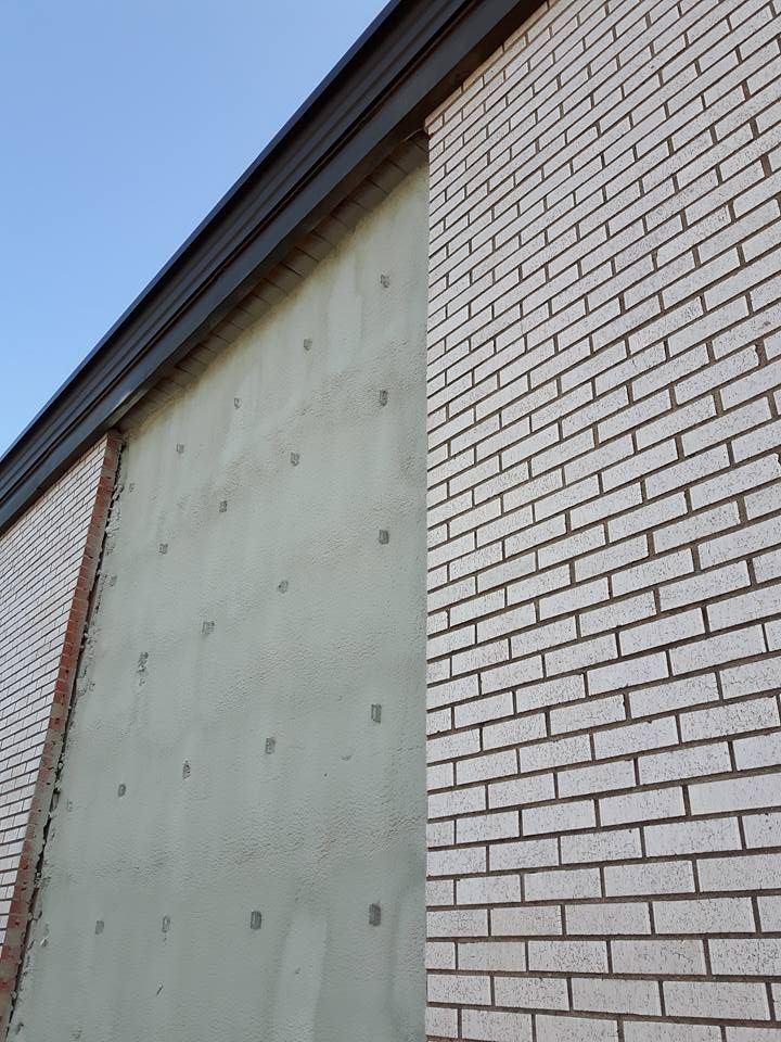 Bâtiment en briques claires avec une section de stuc gris et des attaches.