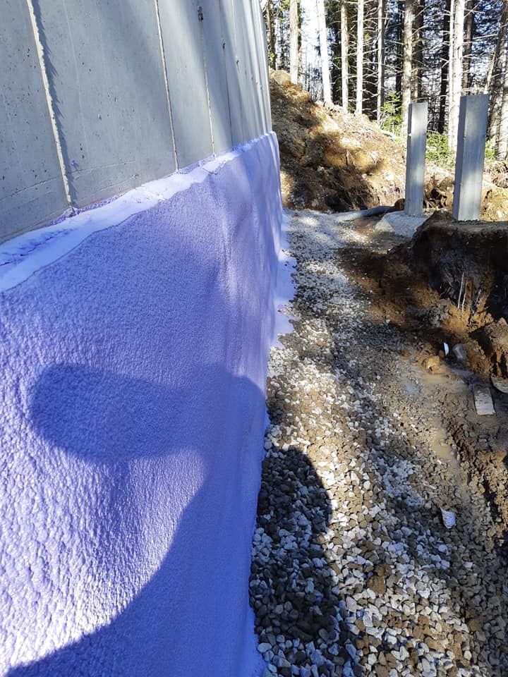 Isolation violette sur un mur de béton, à côté d'un chemin de gravier, dans une zone boisée.