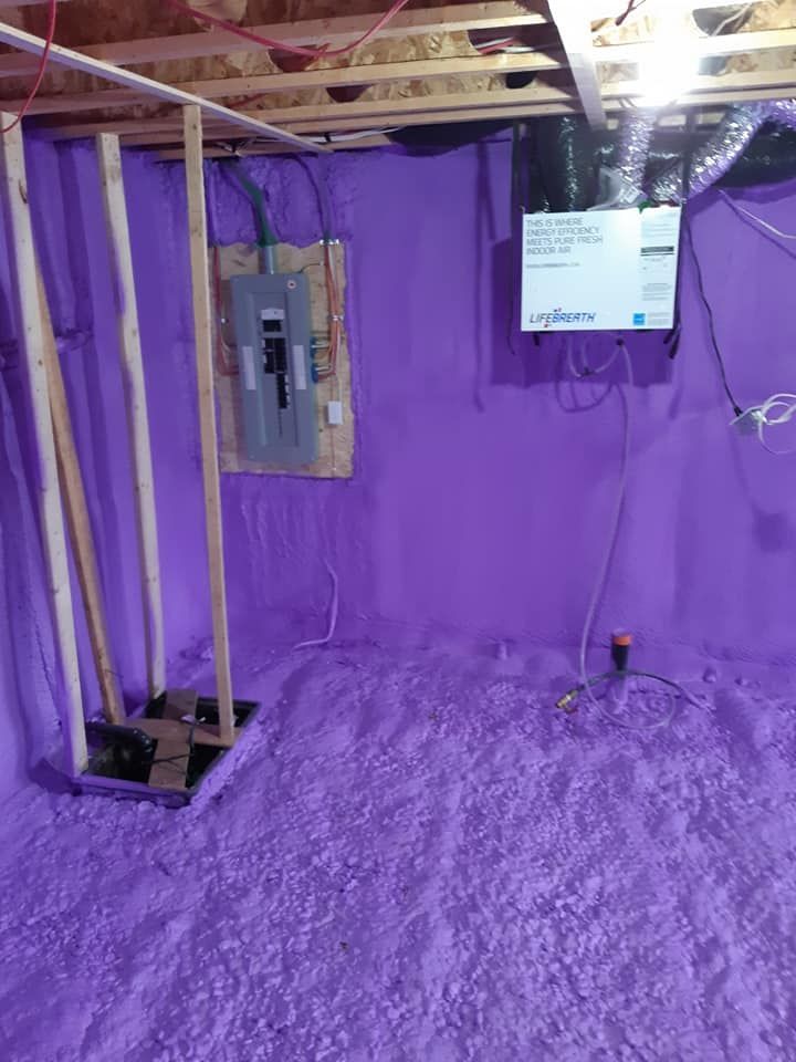 Sous-sol isolé violet avec panneau électrique, charpente en bois et plafond exposé.