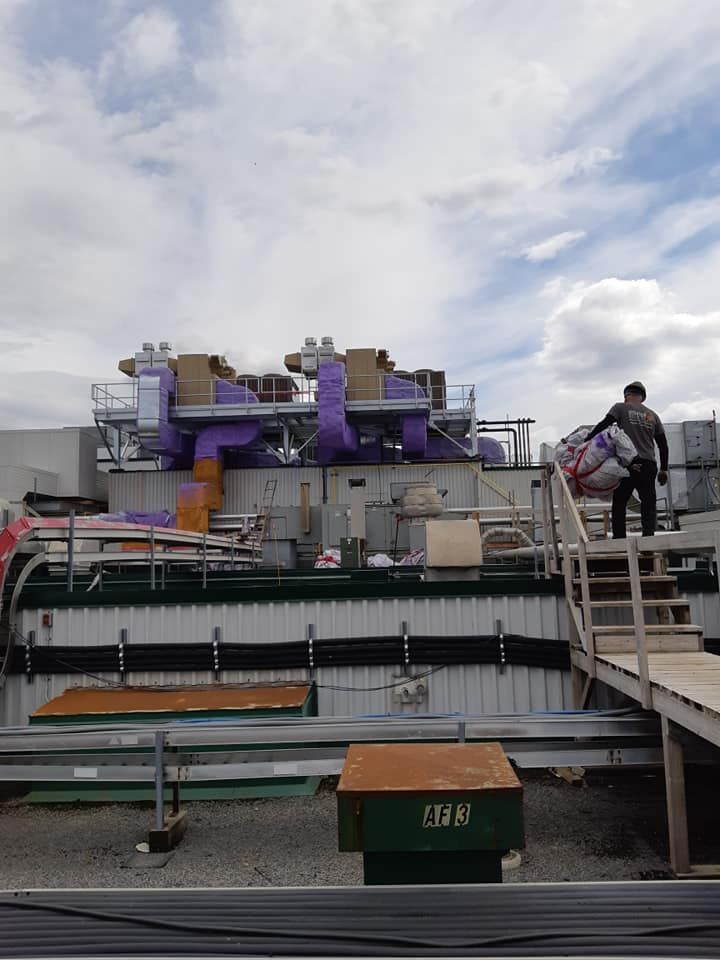 Un homme monte des escaliers en bois vers une grande structure industrielle violette et beige sous un ciel nuageux.