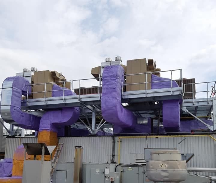 Système CVC sur le toit avec conduits violets isolés et structure en métal argenté, ciel nuageux en arrière-plan.