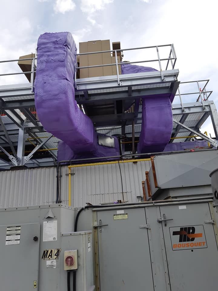 Conduits de CVC violets et isolés sur un toit, boîtiers sur une plateforme métallique. Machines grises en dessous.