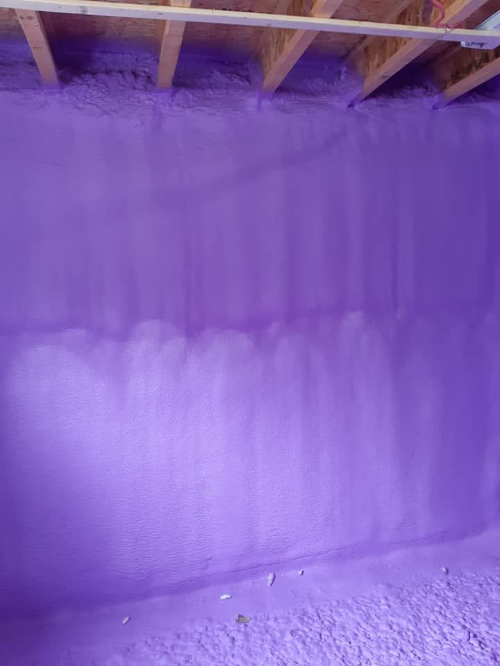 Une isolation en mousse pulvérisée violette recouvre un mur et un plafond dans une pièce à ossature en bois.
