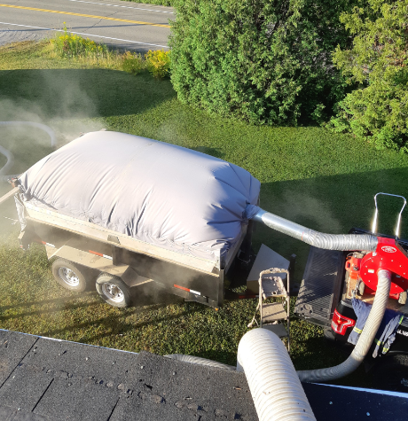Une remorque avec un sac gris rempli, relié à un souffleur, soufflant le matériau sur l'herbe.