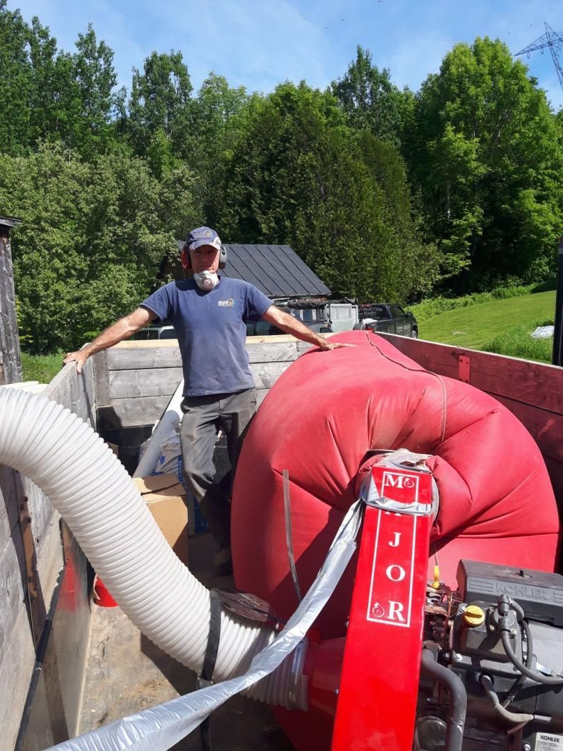 Homme debout, les bras tendus, près d'un ventilateur d'isolation rouge dans la benne d'un camion, à l'extérieur, journée ensoleillée.