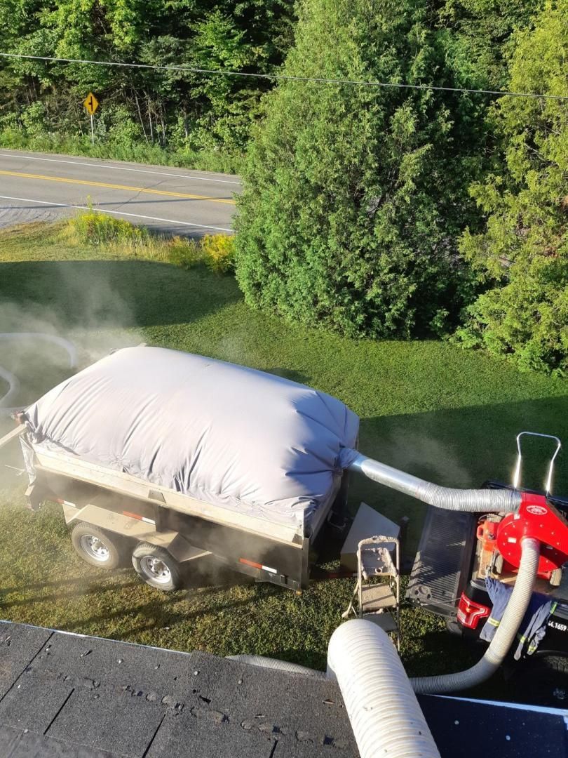 Une remorque avec un grand sac blanc, relié à une machine rouge, soufflant de l'isolant sur un toit.