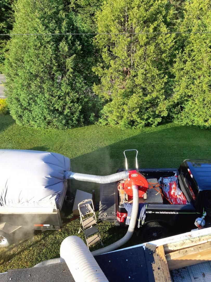 Un camion avec un tuyau de soufflage relié à un conteneur blanc sur un toit, avec une pelouse verte et des arbres en arrière-plan.