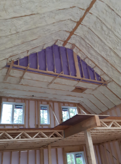 Vue intérieure d'une maison à ossature bois avec isolation en mousse projetée. Le pignon est rempli de mousse violette.