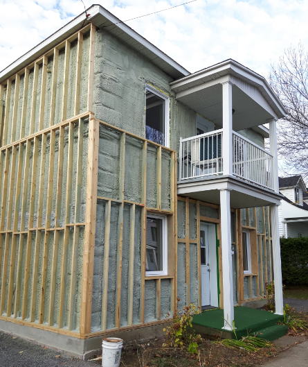 Extérieur de la maison en construction avec charpente apparente, isolation et un petit balcon.