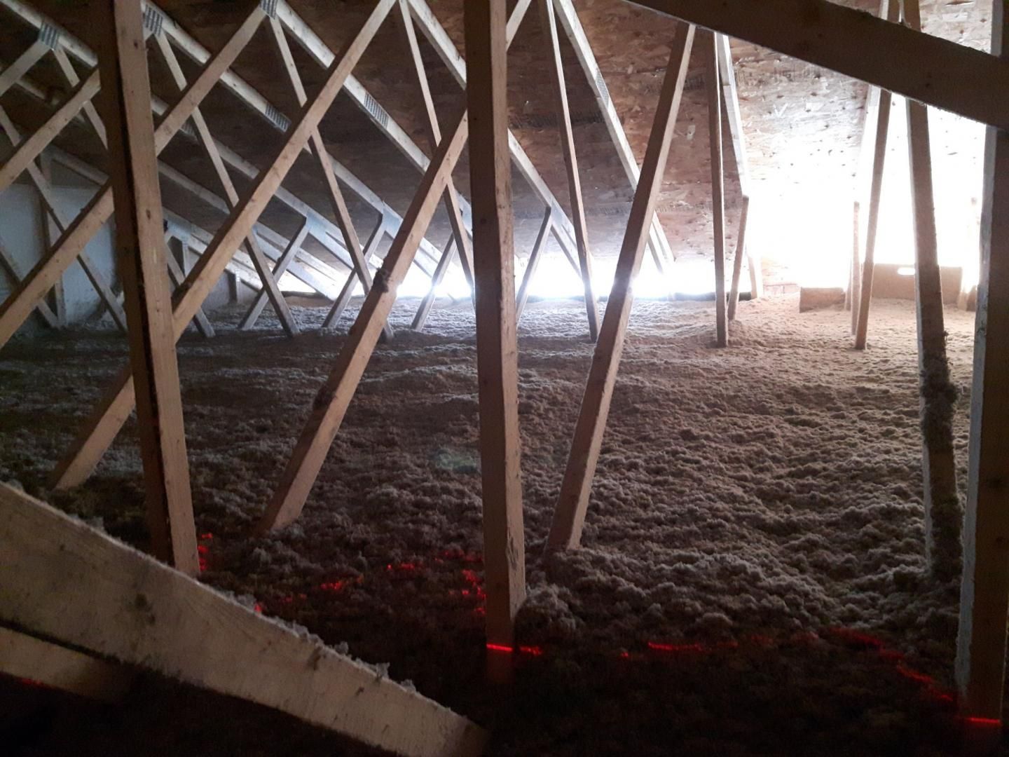 Un grenier avec poutres en bois et isolation; une lumière vive au fond.