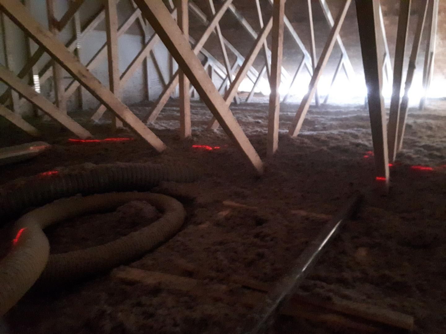 Combles avec poutres en bois, isolation et lignes laser rouges au sol.