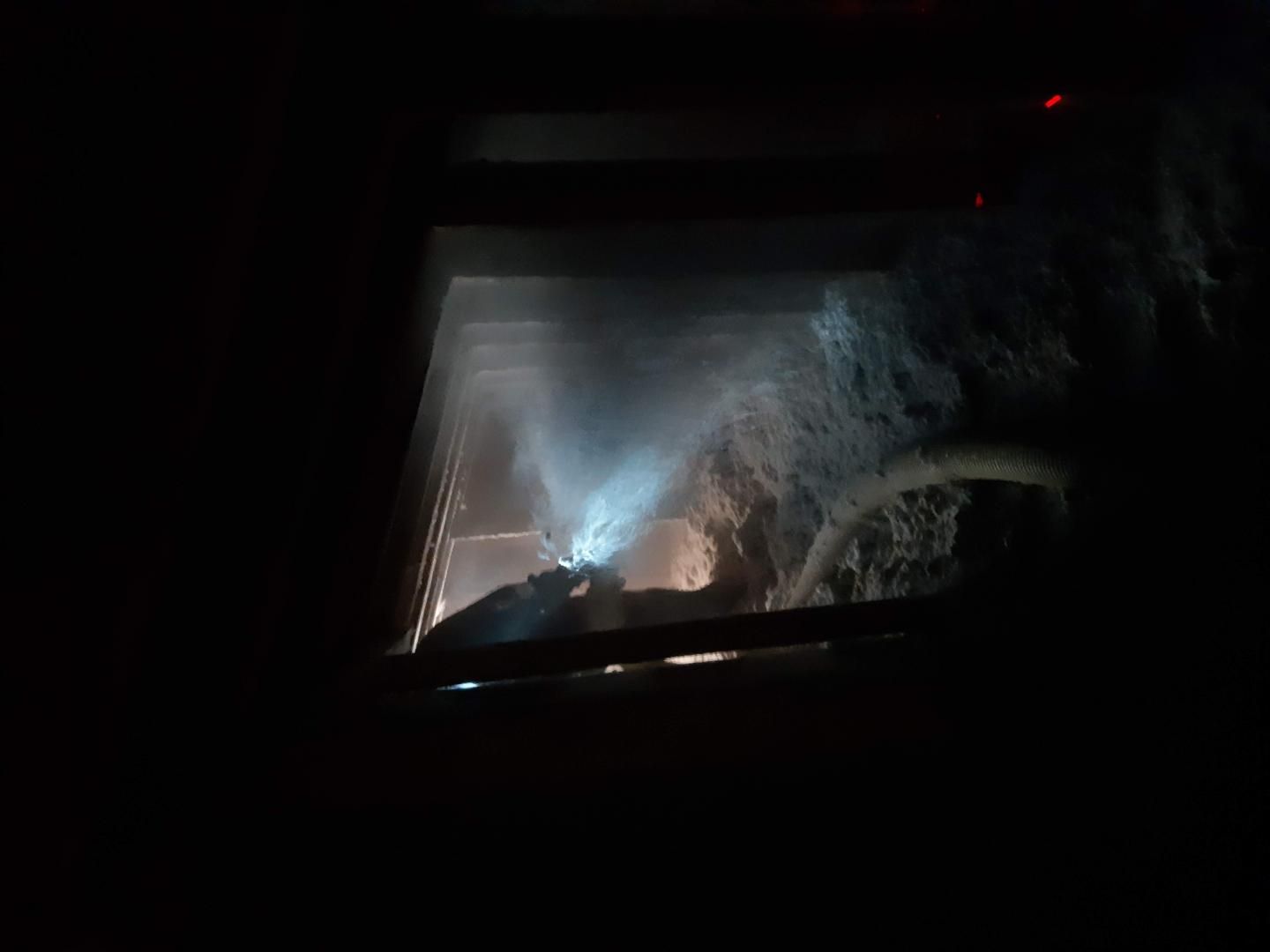 Vue d'une cheminée faiblement éclairée avec de la fumée, du feu et un intérieur partiellement visible.