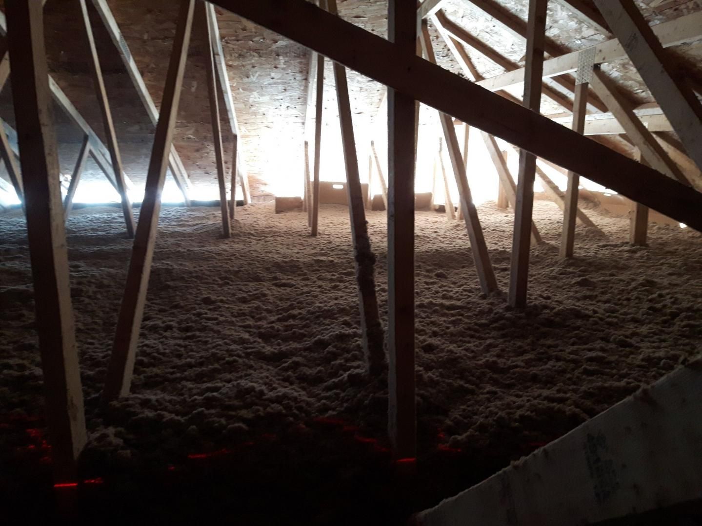 Grenier rempli d'isolant en vrac, de chevrons et de supports en bois ; la lumière naturelle coule d'une fenêtre.