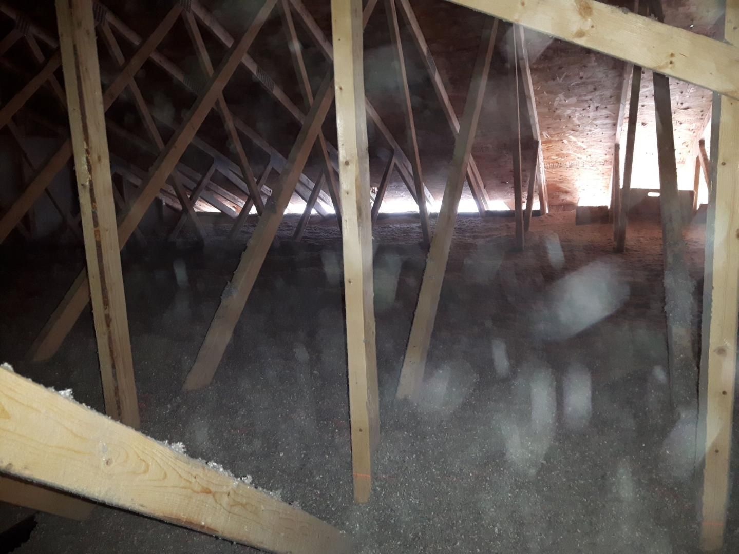 Grenier avec poutres apparentes, isolation poussiéreuse et lumière qui entre.