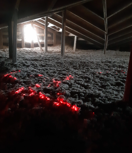 Intérieur du grenier avec isolation et spots rouges lumineux, la lumière du soleil brille à travers une fenêtre.