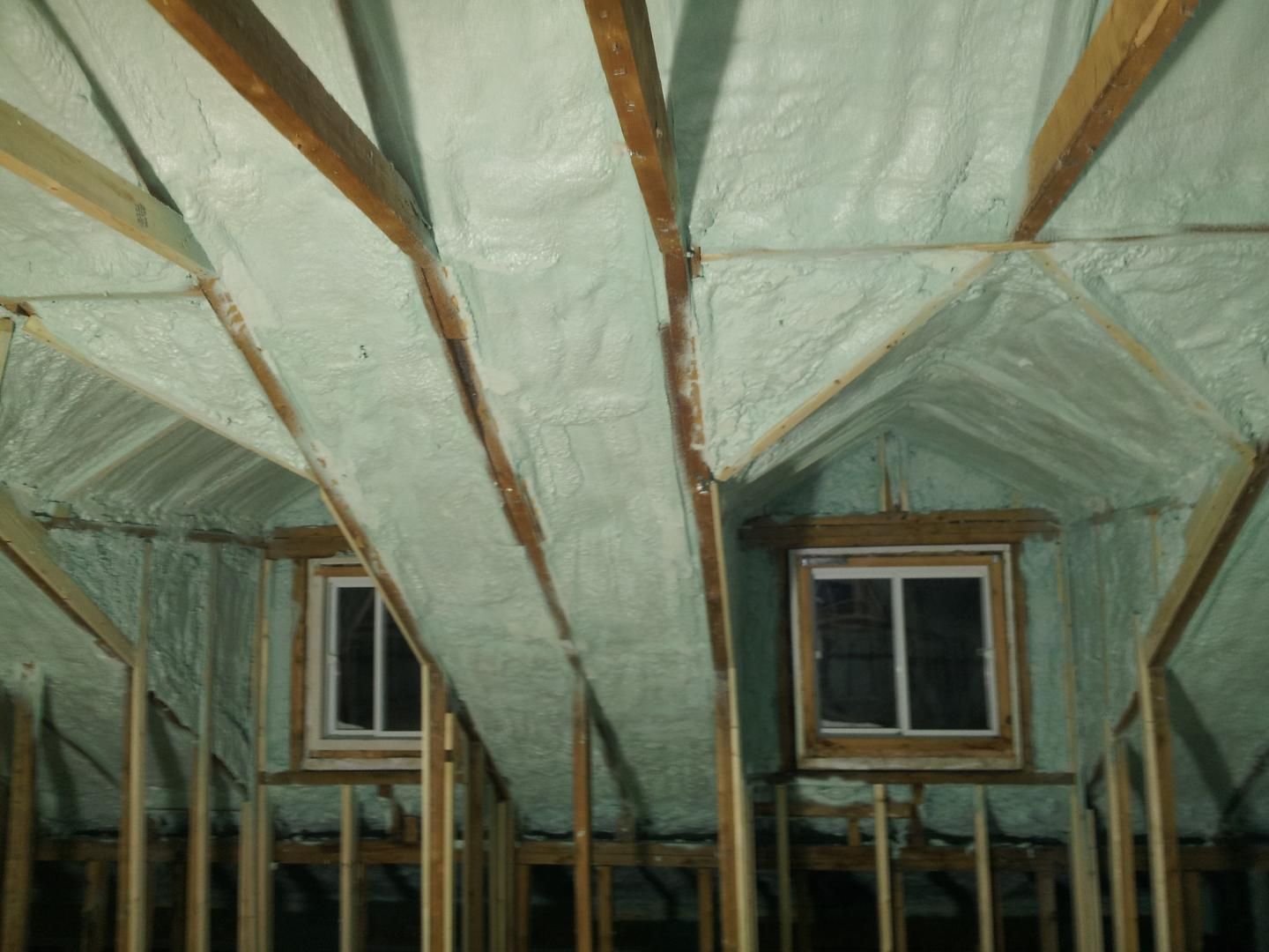 Combles avec ossature bois et isolation en mousse projetée vert clair. Deux fenêtres sont visibles.