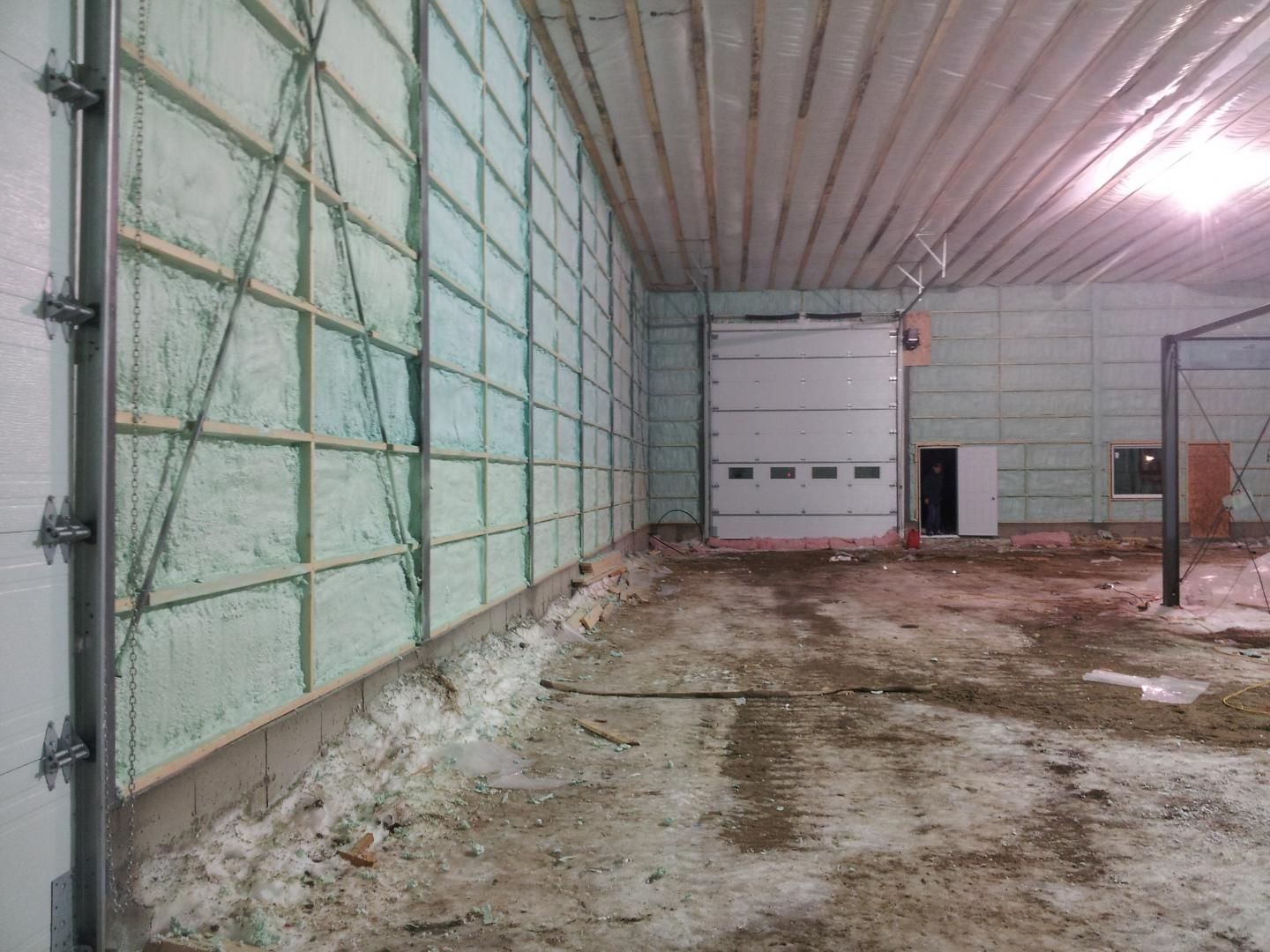 Intérieur d'un bâtiment avec isolation en mousse projetée sur les murs. Porte de garage et sol en béton.