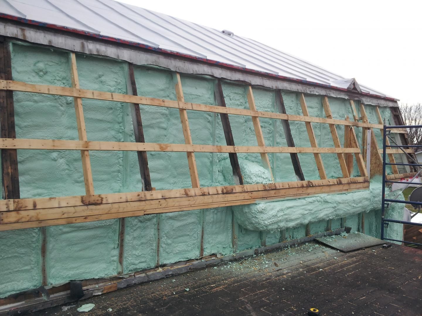 Isolation en mousse verte appliquée à l'extérieur d'un bâtiment, entre des poutres en bois.