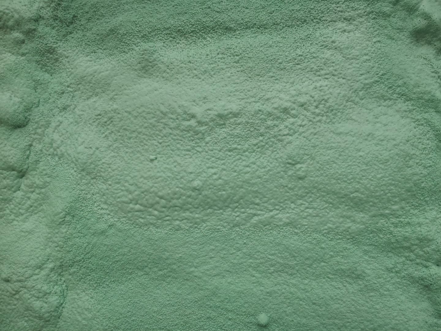 Substance granuleuse vert pâle, peut-être sous forme de poudre ou d'engrais, répartie uniformément.