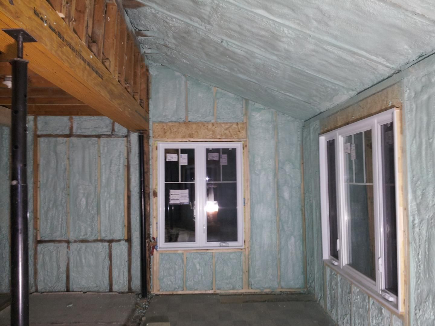 Intérieur d'une pièce en construction avec isolation en mousse pulvérisée sur les murs et le plafond, les fenêtres sont installées.